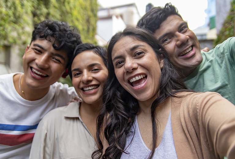 Día Internacional de la Alegría Cuatro jóvenes sonríen mientras se hacen un selfie al aire libre.