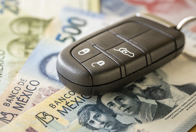 Protección sobre ruedas Llave electrónica de automóvil colocada sobre billetes mexicanos de 500 pesos, representando el coste económico de los incidentes viales y la importancia del seguro de auto para la protección financiera.