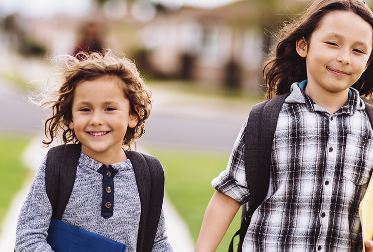 La vuelta al cole Dos niños con mochilas caminando juntos hacia el colegio.