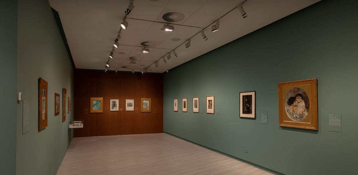 Día Internacional de los Museos Sala de museo con paredes verdes y marrones, varias obras enmarcadas expuestas a ambos lados, iluminación de galería y un cuadro destacado en primer plano.